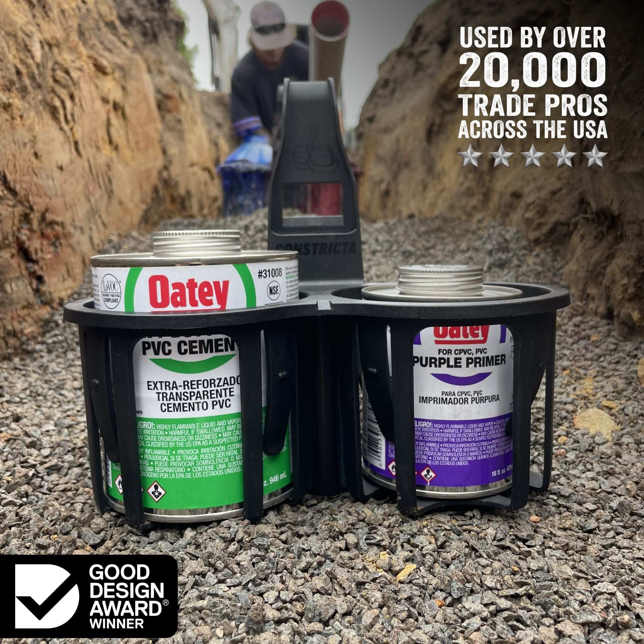 Oatey PVC Cement and Purple Primer cans in a constricta multi-pot grip shown outdoors on gravel with a trench and a person in the background. Text on the image reads 'USED BY OVER 20,000 TRADE PROS ACROSS THE USA' and includes a 'Good Design Award Winner' badge.