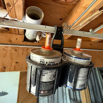 Two cans of PVC cement held by Rebend Constricta Glue Pot Grip against a wooden wall.