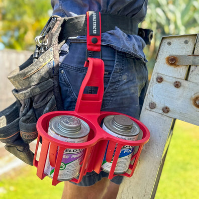 Red spray Constricta Glue Pot Multi Grip on a person's waist with Primer cans attached, outdoors.